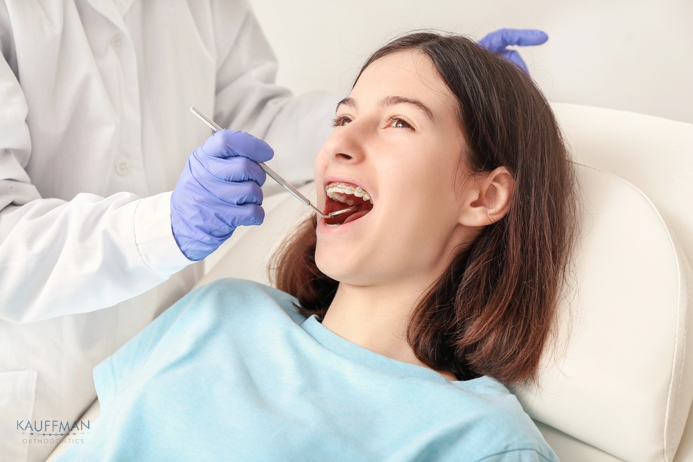 Orthodontist examining a young woman’s teeth during a dental appointment, highlighting routine orthodontic care after understanding about How Long Do Braces Take in New Braunfels, TX.