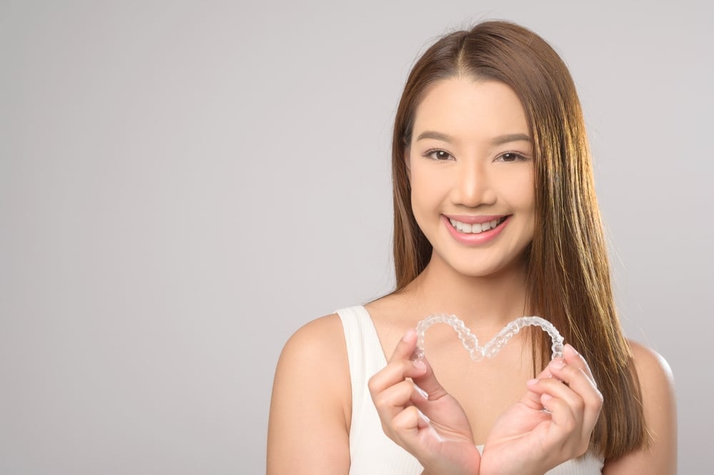 young smiling woman holding invisalign clear aligners - Can Invisalign Fix Overbite in New Braunfels, TX.