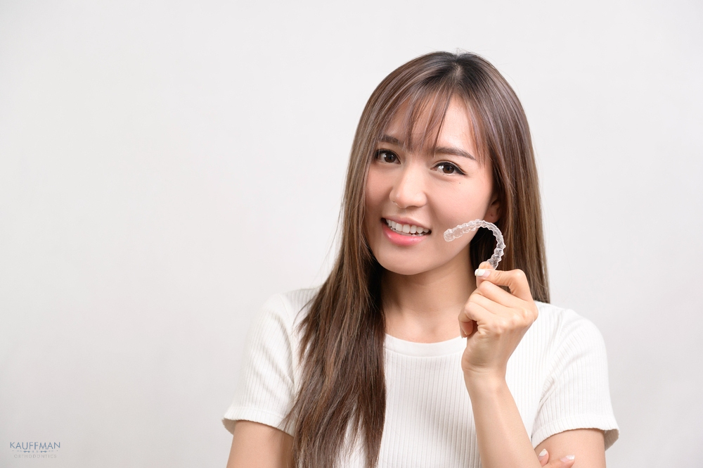 young smiling woman holding invisalign clear aligners white background - Aligners vs Braces in New Braunfels, TX 